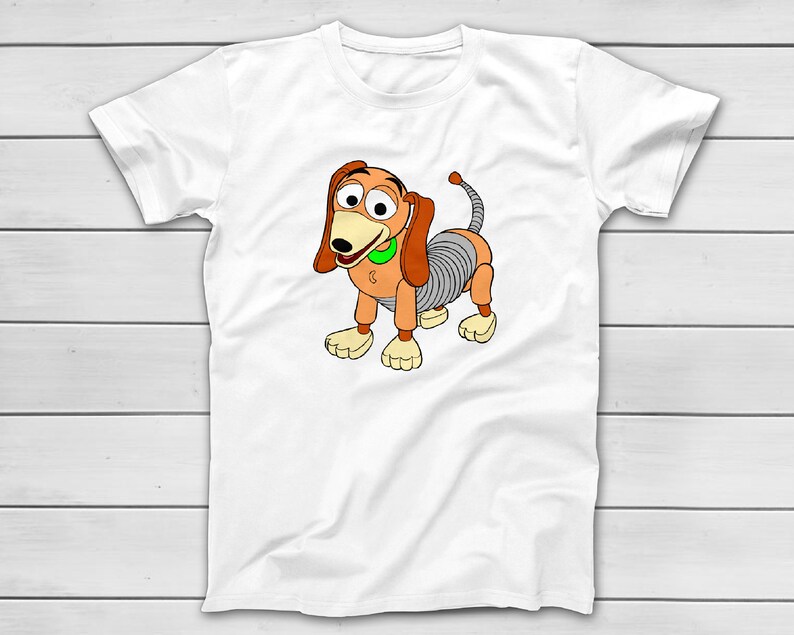 Puede incluir: Camiseta blanca con una ilustraci&oacute;n de dibujos animados de Slinky Dog de Toy Story. El perro est&aacute; representado en tonos marrones, beige y grises, con un collar verde. El dise&ntilde;o est&aacute; centrado en la camiseta.