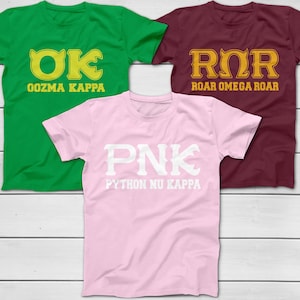 Peut inclure: Trois t-shirts à manches courtes, verts, bordeaux et roses. Chaque chemise présente un design différent dans des couleurs contrastées. Le t-shirt vert dit "OK Oozma Kappa", le t-shirt bordeaux dit "ROR Roar Omega Roar", et le t-shirt rose dit "PNK Python Nu Kappa".
