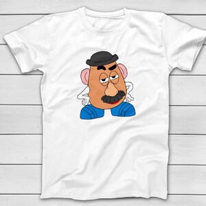 Puede incluir: Camiseta blanca con una ilustraci&oacute;n de dibujos animados de Mr. Potato Head. El personaje tiene una cara bronceada, un bigote negro y lleva un bomb&iacute;n negro y zapatos azules. El dise&ntilde;o est&aacute; centrado en la camiseta.