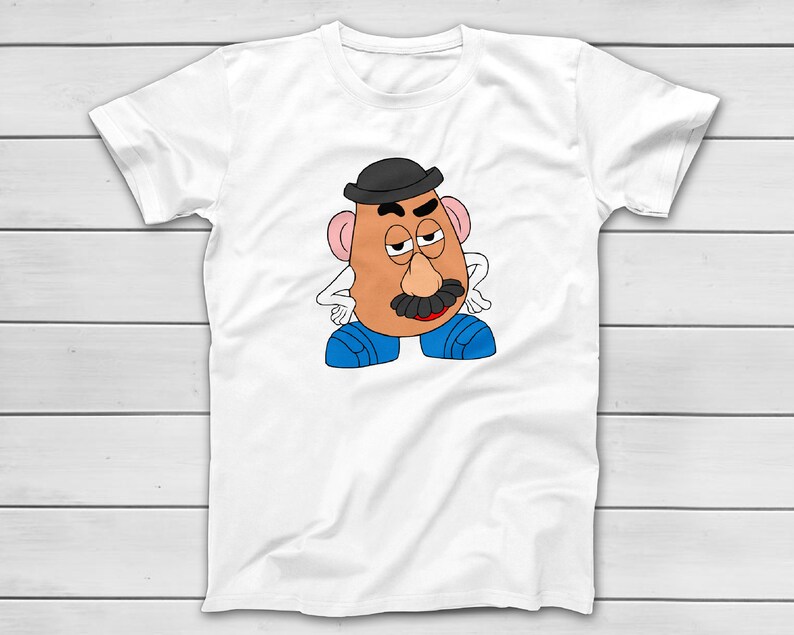 Puede incluir: Camiseta blanca con una ilustraci&oacute;n de dibujos animados de Mr. Potato Head. El personaje tiene una cara bronceada, un bigote negro y lleva un bomb&iacute;n negro y zapatos azules. El dise&ntilde;o est&aacute; centrado en la camiseta.