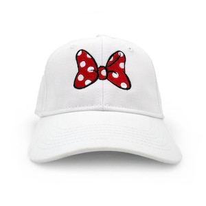 May include: A white baseball cap featuring a red bow with white polka dots. The bow is embroidered on the front of the cap. The cap has a curved brim and a structured design.