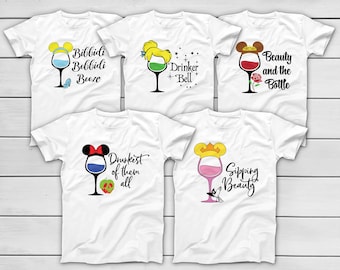 May include: White t-shirts with wine glass designs featuring cartoon character elements and phrases like "Bibbidi Bobbidi Booze" and "Drinker Bell." Each shirt has a unique design with different colors and text.