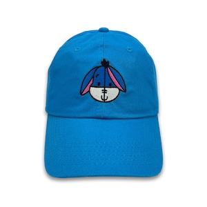 May include: A bright blue baseball cap featuring an embroidered image of Eeyore from Winnie the Pooh. The cap has a curved brim and a six-panel design. The Eeyore image includes blue, pink, and white details.
