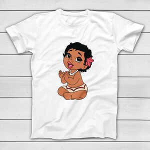 Puede incluir: Camiseta blanca con una ilustraci&oacute;n de dibujos animados de una ni&ntilde;a con piel oscura, cabello negro y una flor rosa. El beb&eacute; est&aacute; sentado con las piernas cruzadas, aplaudiendo y usando un collar blanco y un pa&ntilde;al estampado.