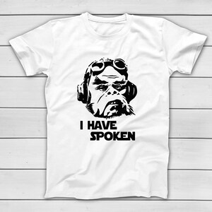 May include: White t-shirt with a black graphic of a character wearing goggles and headphones. The text "I HAVE SPOKEN" is printed below the image. The shirt is made of a soft material.