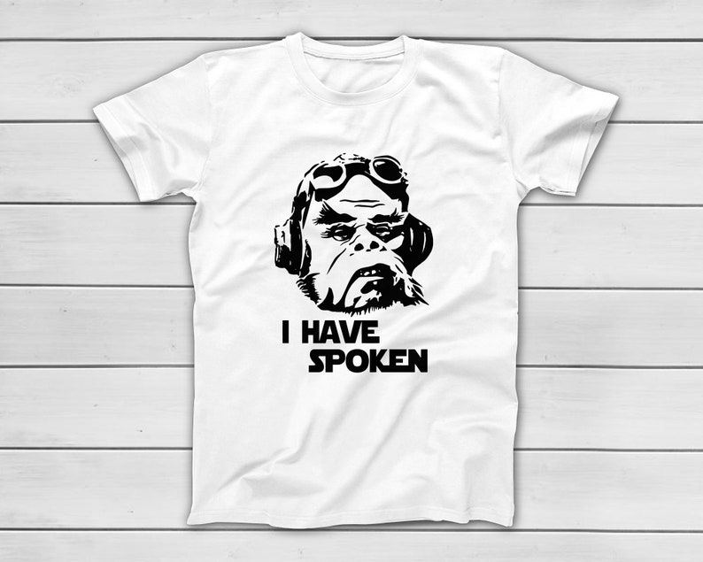 May include: White t-shirt with a black graphic of a character wearing goggles and headphones. The text "I HAVE SPOKEN" is printed below the image. The shirt is made of a soft material.