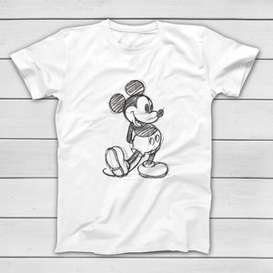 Puede incluir: Camiseta blanca con un boceto en blanco y negro de Mickey Mouse. El personaje de dibujos animados est&aacute; representado en una pose cl&aacute;sica, con las manos a la espalda y una expresi&oacute;n alegre. La camiseta est&aacute; hecha de un material suave.