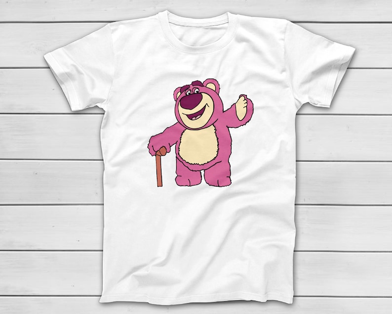 Puede incluir: Camiseta blanca con una ilustraci&oacute;n de dibujos animados de un oso rosa con un bast&oacute;n marr&oacute;n. El oso est&aacute; sonriendo y saludando. El dise&ntilde;o est&aacute; impreso en la parte delantera de la camiseta.