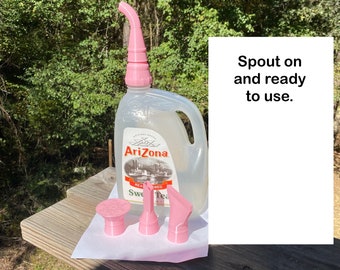 May include: A clear plastic Arizona Sweet Tea jug with a pink screw-on spout attached to the top. Three additional pink plastic attachments of varying shapes are placed in front of the jug. The text Spout on and ready to use is visible.