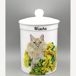 May include: White ceramic storage jar with a lid and a round handle. The jar is decorated with a hand-painted image of a fluffy cat and yellow flowers. The name "Mischa" is written in black script above the cat.