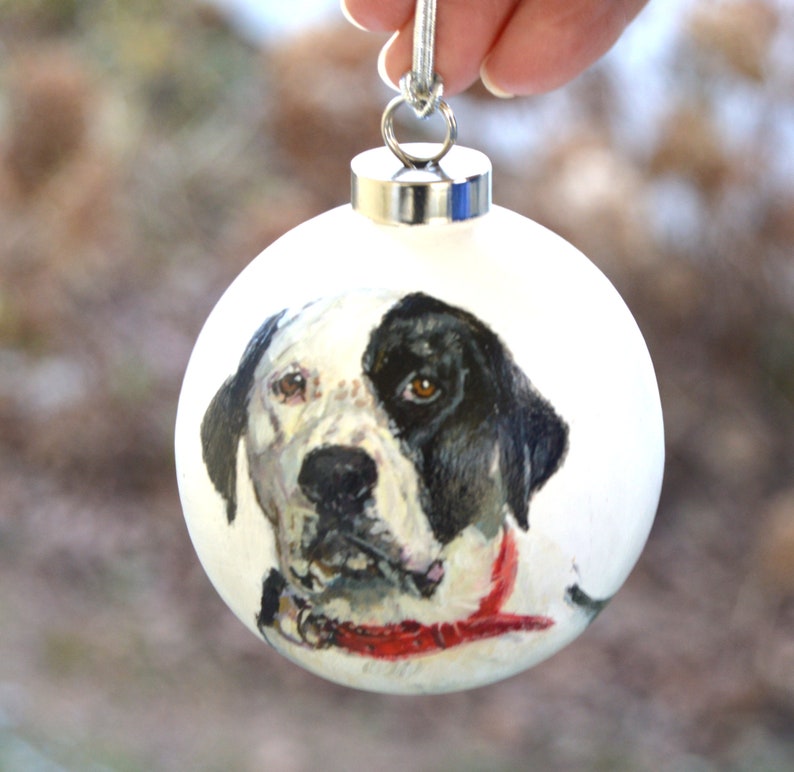 Pode incluir: Ornamento de Natal branco com um retrato pintado &agrave; m&atilde;o de um c&atilde;o preto e branco usando uma bandana vermelha.