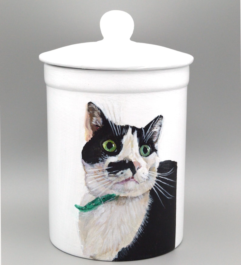 May include: A white ceramic mug with a black handle and the text "But First, Coffee" in a black, bold font. The mug is on a white surface. The mug is approximately 10 cm tall.