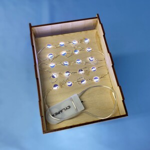 May include: A set of white LED fairy lights in a wooden box with a battery pack labelled "CYLAPEX".