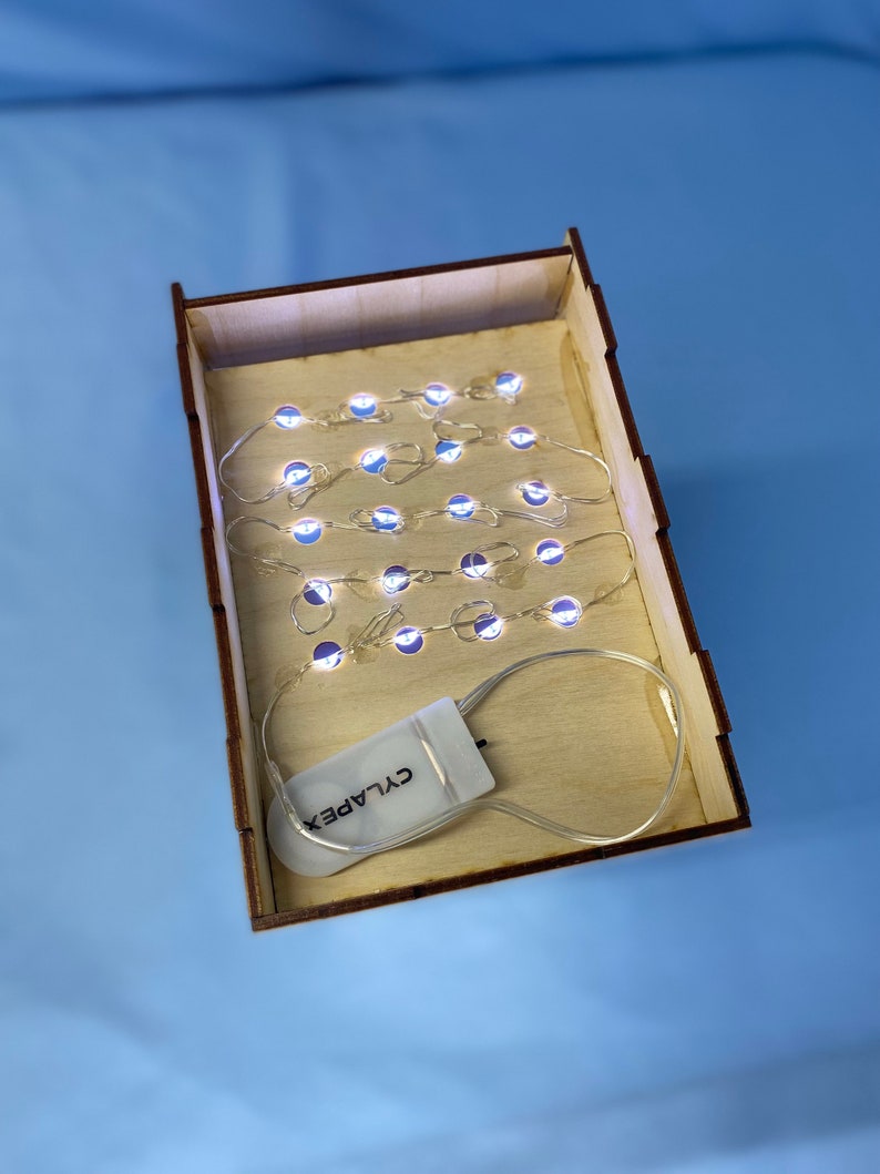 May include: A set of white LED fairy lights in a wooden box with a battery pack labelled "CYLAPEX".
