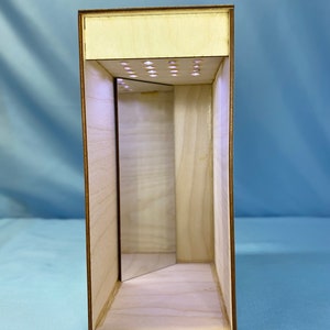 May include: A wooden box with a mirror inside and a row of small lights on the top. The box is made of light wood and has a natural finish.