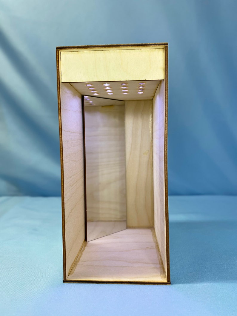 May include: A wooden box with a mirror inside and a row of small lights on the top. The box is made of light wood and has a natural finish.