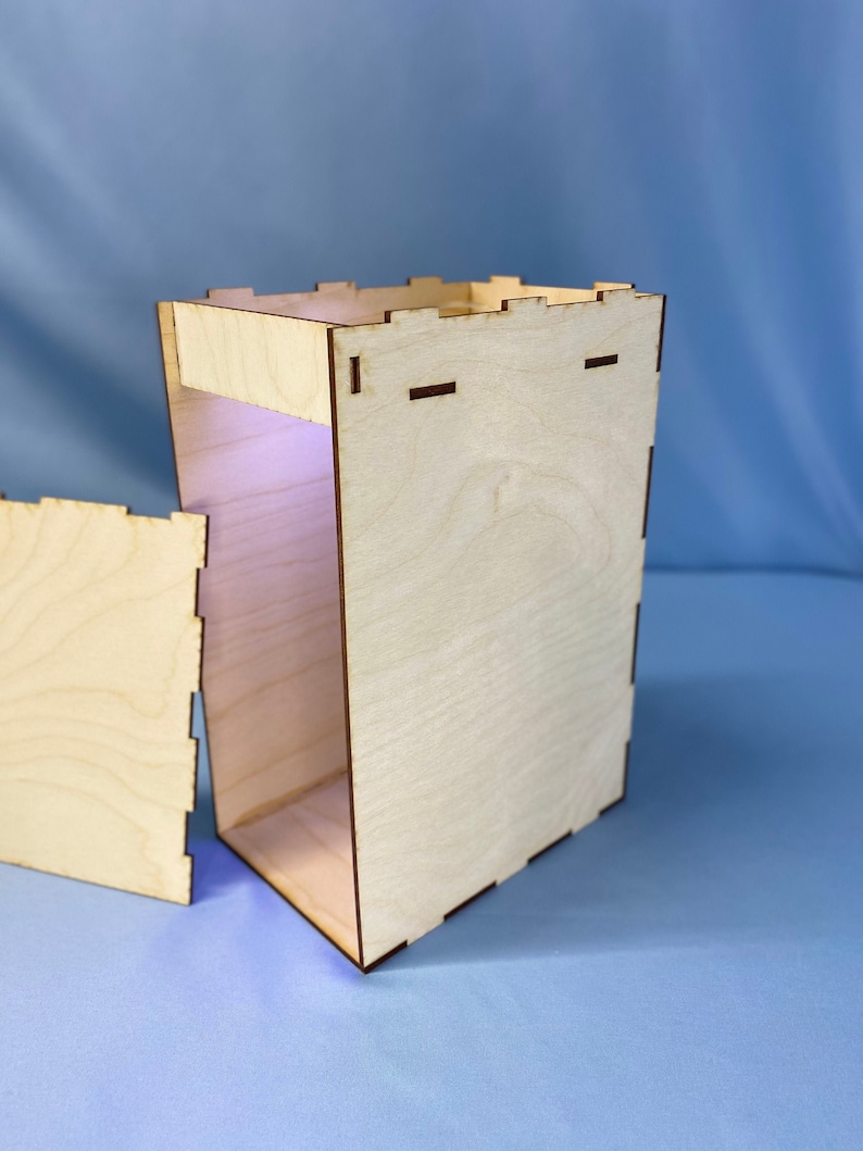 May include: An open wooden box with a light brown finish. The box is made of plywood and has a simple design. The box is open and the inside is visible.