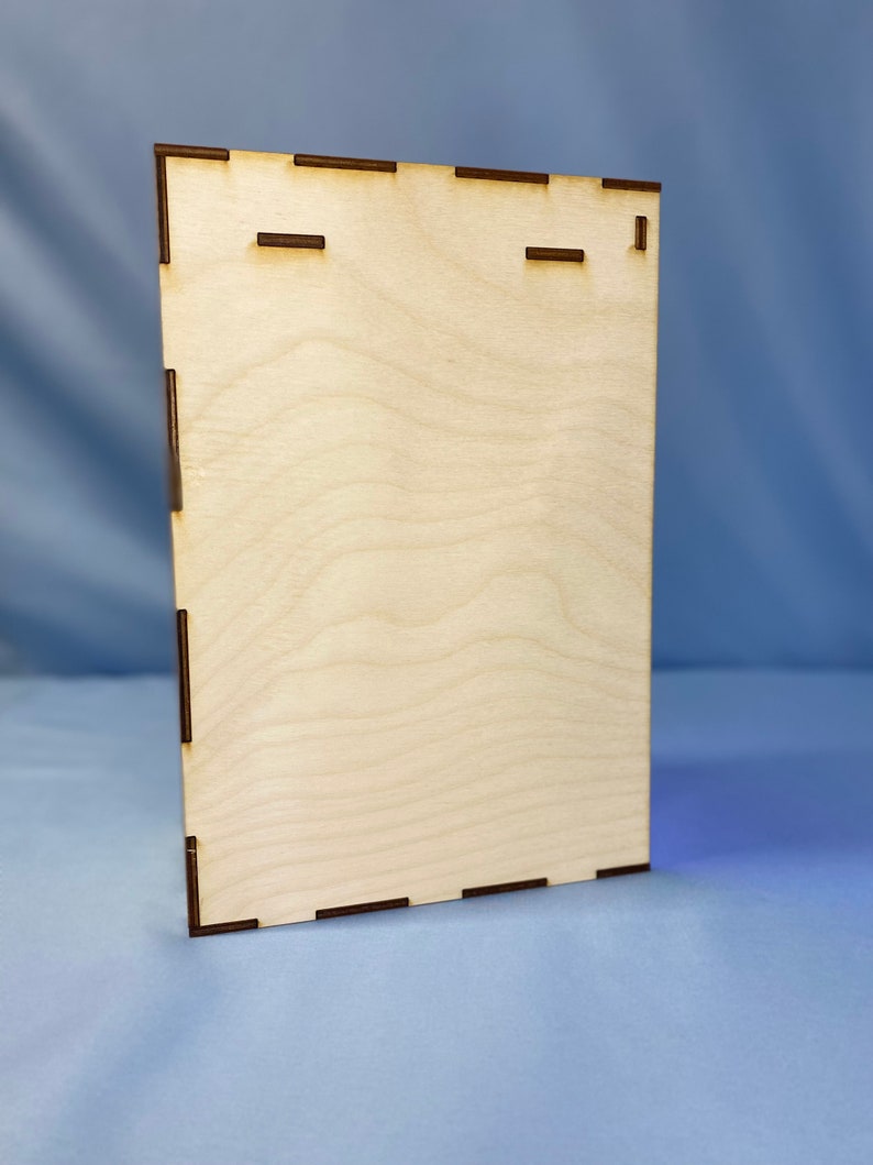 May include: A plain, light brown wooden plaque with a rectangular shape and a smooth surface. The plaque has two small, rectangular cutouts near the top.