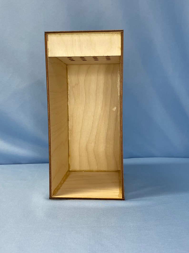 May include: A wooden box with a removable top and a series of small holes in the top. The box is empty and has a light brown finish.