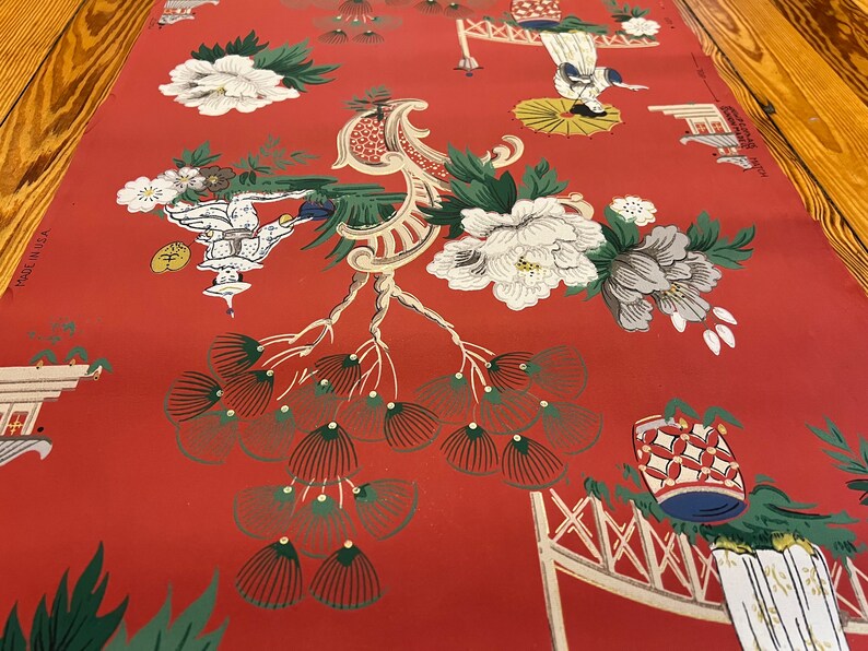May include: A red wallpaper featuring a repeating pattern of white and grey peonies, stylized green pine trees, and figures holding umbrellas. The design includes architectural elements and text that reads MADE IN U.S.A. and STRIP MATCH.