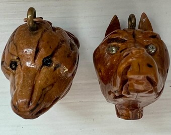 May include: Two carved wooden animal head pendants. One is a bear with black eyes, and the other is a horse with rhinestone eyes. Both have a brass loop at the top for hanging.