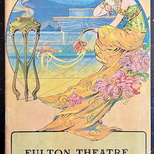 May include: Vintage Fulton Theatre program cover featuring an Art Nouveau illustration. A woman in a flowing yellow gown and green top sits near a decorative stand. The background includes a blue sky and water. Text reads "FULTON THEATRE".