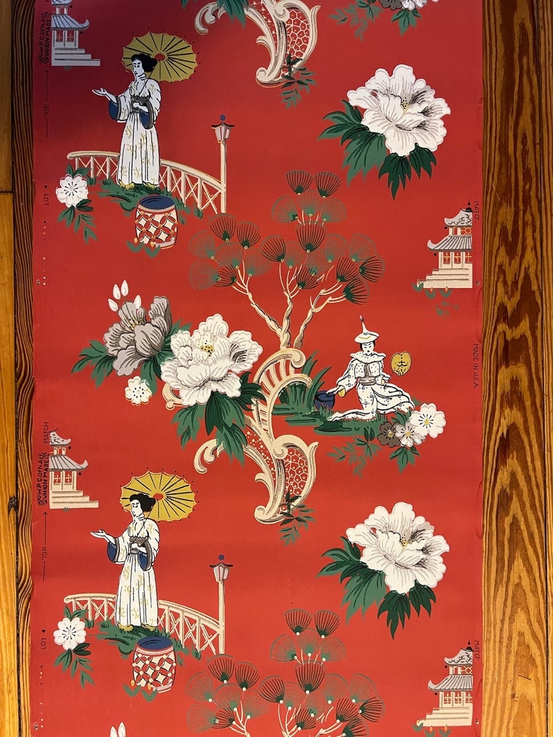 May include: A roll of wallpaper with a vibrant red background featuring a repeating pattern of figures holding yellow umbrellas, white pagodas, large white peony flowers, and green pine trees. The text "MADE IN U.S.A." is printed on the side.
