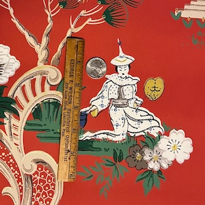 May include: A red wallpaper featuring a repeating pattern of a figure in white robes holding a yellow fan, surrounded by white flowers and green trees. A wooden ruler measuring 6 inches and a silver coin are placed on the surface for scale.