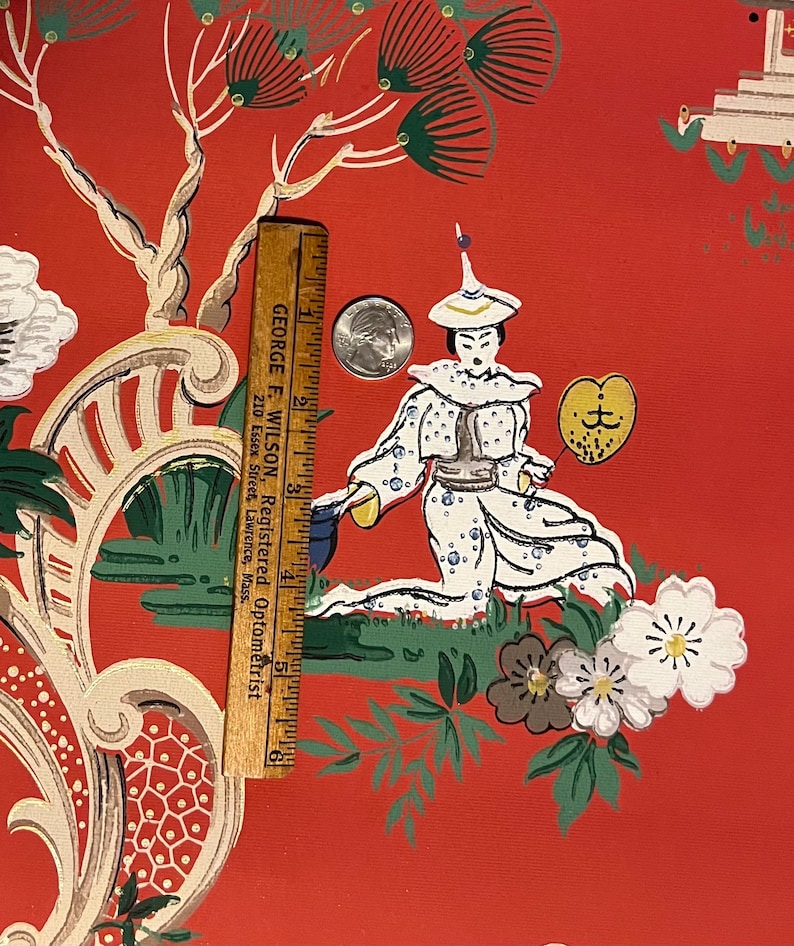 May include: A red wallpaper featuring a repeating pattern of a figure in white robes holding a yellow fan, surrounded by white flowers and green trees. A wooden ruler measuring 6 inches and a silver coin are placed on the surface for scale.