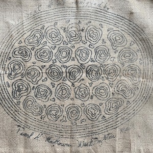May include: A tan fabric with a hand-drawn design of an oval shape filled with circular patterns. The design is outlined in black ink. Text is visible at the bottom of the image.