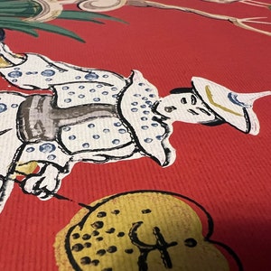 May include: A red textured surface featuring a painted illustration of a figure wearing a white garment with blue polka dots and a wide-brimmed hat. The figure holds a blue vessel and a yellow fan with black markings, set against a vibrant red background.