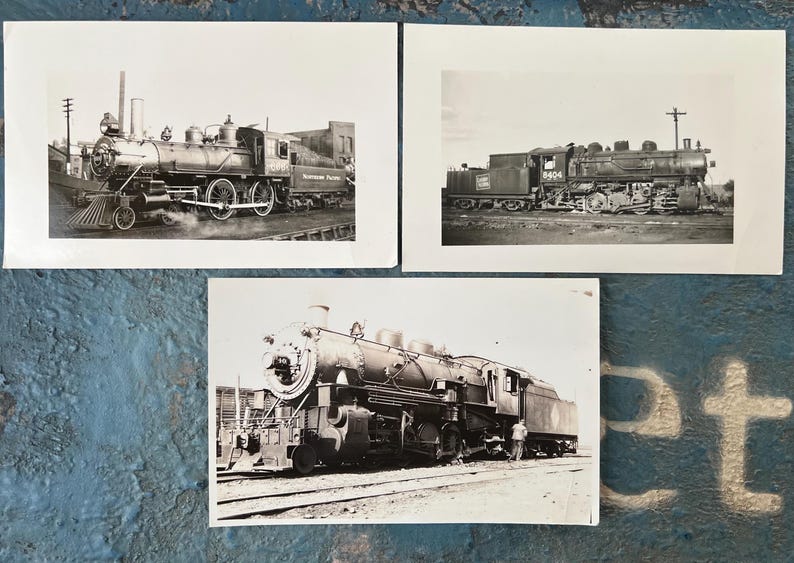 May include: Three black and white photographs of steam locomotives. The images show the trains from different angles, highlighting their intricate details. The locomotives are on tracks, with some smoke visible, suggesting they are in operation. The photographs are on white paper.