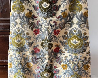 May include: A long, cream-colored skirt with an ornate floral pattern. The design features repeating motifs in shades of green, gray, red, and yellow. The skirt is made of a soft, velvety fabric, and is hanging on a hanger.