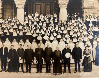 May include: A sepia-toned photograph of a large group of people posing on stone steps. The group includes many individuals wearing religious habits and veils, and several men in dark suits. The text at the bottom reads: SUMMER SCHOOL CATHOLIC UNIVERSITY OF AMERICA 1914.