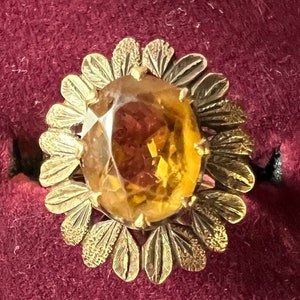 May include: A gold ring with a large, faceted, amber-colored gemstone set in a flower-shaped design.