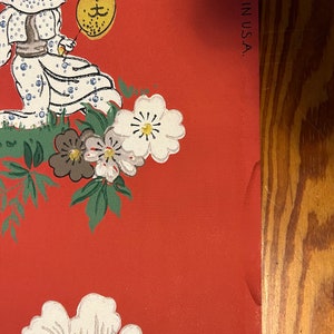 May include: A red wallpaper featuring a repeating pattern of a person in a white dotted outfit holding a yellow fan, surrounded by white and brown flowers with green leaves. The text MADE IN U.S.A. is printed vertically along the right edge.