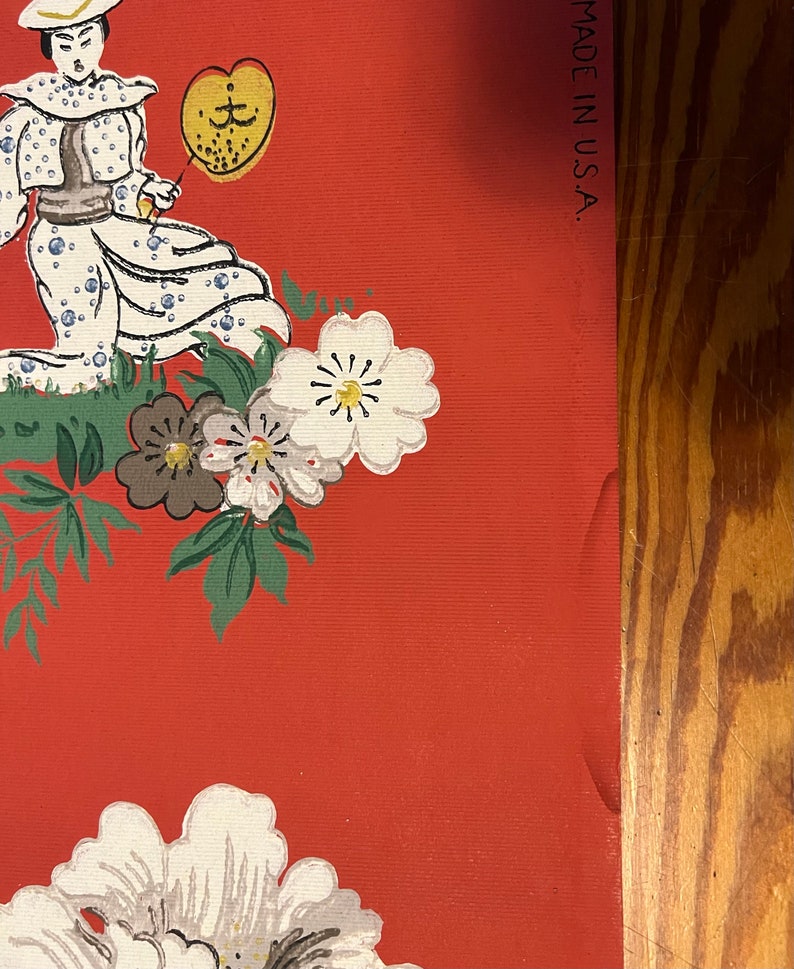 May include: A red wallpaper featuring a repeating pattern of a person in a white dotted outfit holding a yellow fan, surrounded by white and brown flowers with green leaves. The text MADE IN U.S.A. is printed vertically along the right edge.