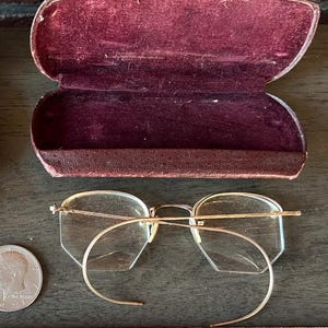 May include: A pair of vintage gold-rimmed glasses with octagonal lenses and a thin gold wire frame. The glasses are in a burgundy velvet-lined case.