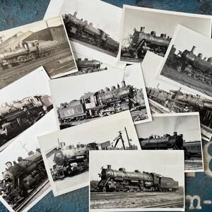 May include: A collection of black and white photographs featuring steam locomotives. The images showcase various angles and details of the trains, including their wheels, cabs, and overall design. The photographs are arranged on a textured blue surface.