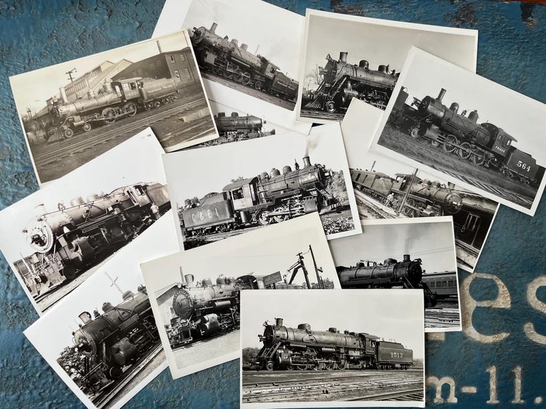 May include: A collection of black and white photographs featuring steam locomotives. The images showcase various angles and details of the trains, including their wheels, cabs, and overall design. The photographs are arranged on a textured blue surface.