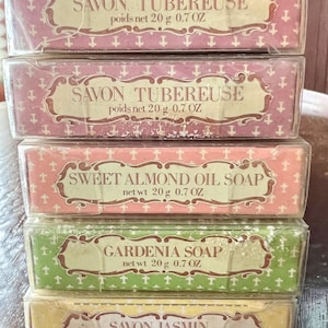 May include: A stack of five rectangular soap bars in individual clear plastic wrappers. The labels feature decorative borders and text including SAVON TUBEREUSE, SWEET ALMOND OIL SOAP, GARDENIA SOAP, and SAVON JASMIN, each marked with 20 g 0.7 OZ.