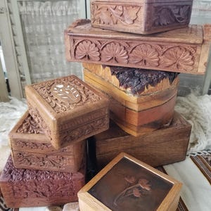 May include: A collection of intricately carved wooden boxes in various sizes and shapes. The boxes feature detailed floral and leaf patterns, with a range of brown tones. Some boxes have a natural wood grain finish, while others are stained a darker color.