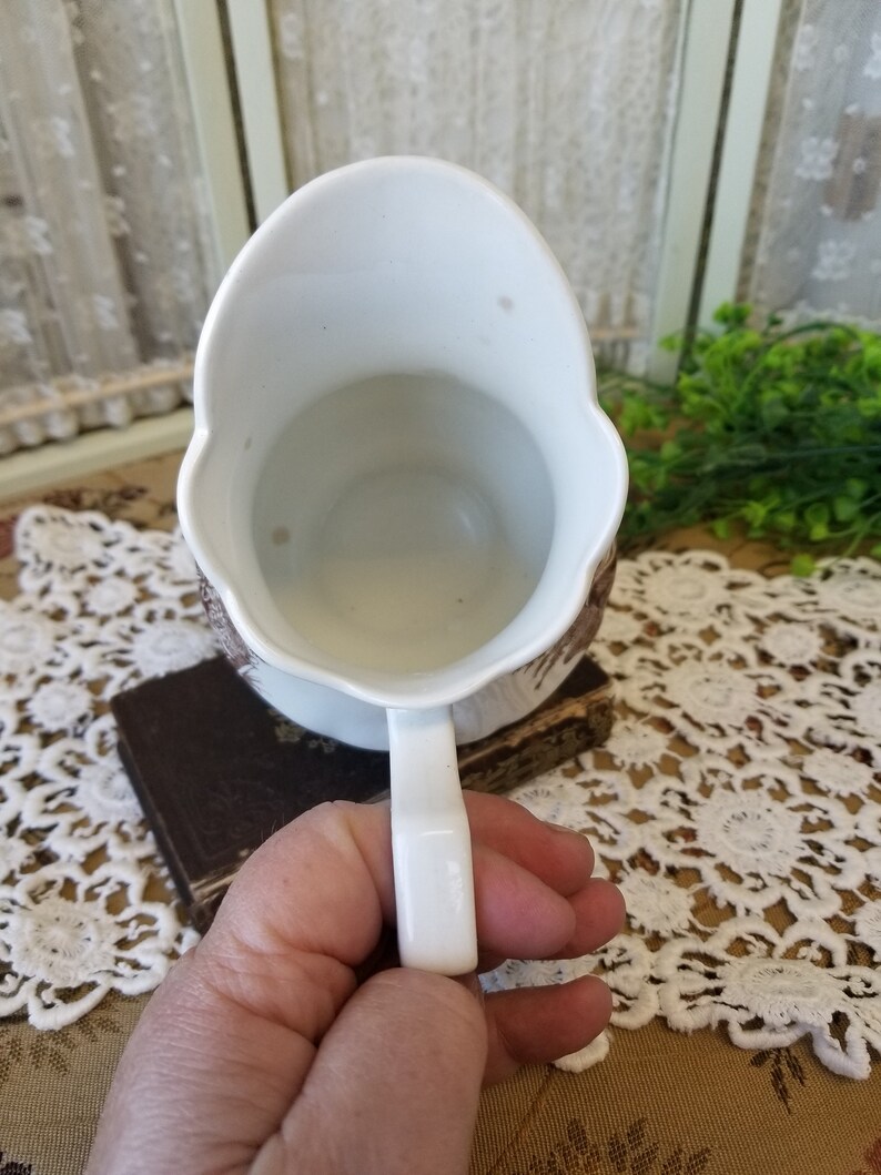 May include: White ceramic pitcher with a brown and white floral design. The pitcher has a handle and a wide mouth.