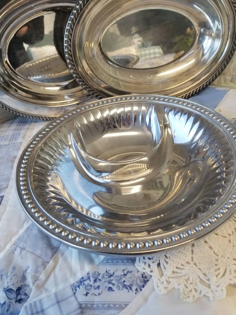 Puede incluir: Un conjunto de fuentes de plata. El juego incluye fuentes ovaladas con bordes de cuerda y una fuente dividida con un borde de cuentas. Las superficies reflectantes crean una apariencia brillante y elegante.