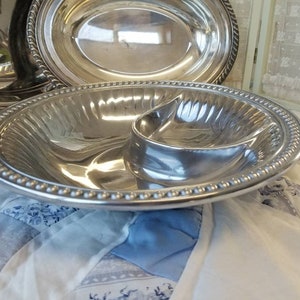 Puede incluir: Un juego de fuentes de plata. El juego incluye una fuente ovalada y una fuente dividida con un peque&ntilde;o compartimento adjunto. Los bordes de las fuentes est&aacute;n decorados con detalles de cuentas y cuerdas. Las fuentes son reflectantes.