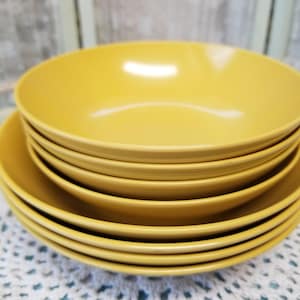 May include: A stack of six yellow ceramic bowls. The bowls are nested inside each other, with the largest bowl on the bottom and the smallest bowl on top.