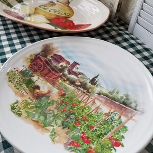 May include: White ceramic serving platter with a painted scene of a tomato garden with red tomatoes, green vines, and a wooden wagon. The text "Oil Oliva" is visible on the platter.