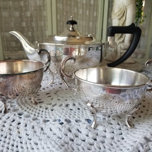 May include: A silver tea set with a teapot, creamer, and sugar bowl. The set has a traditional design with ornate handles and feet.