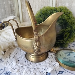 May include: A vintage brass ice bucket with a handle and a decorative lion head design. The bucket is sitting on a white lace doily.
