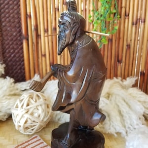 May include: A dark brown wooden sculpture of a man with a long beard and a long robe. The sculpture is standing on a wooden base. The sculpture is in a traditional Chinese style.